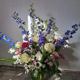 Mixed bouquet of white roses, blue delphinium, and pink flowers in a glass vase