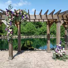 Floral arrangements draped over a wooden pergola beside a pond