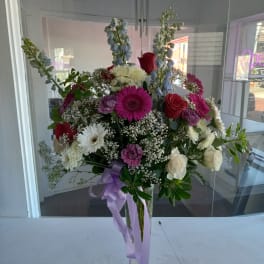 Tall mixed bouquet in a clear vase with purple ribbon