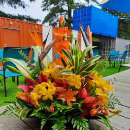 Tropical floral arrangement with orange, yellow, and red blooms in a low container