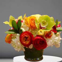 Colorful bouquet of ranunculus, orchids, and hydrangeas in a dark vase