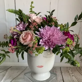 Pink and lavender flowers arranged in a white face vase