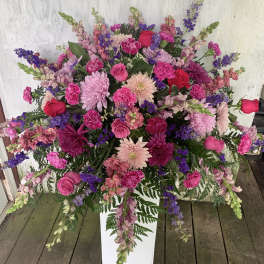 Large pink and purple floral arrangement in a white pedestal vase