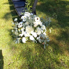 White floral arrangement on grass beside a row of black chairs