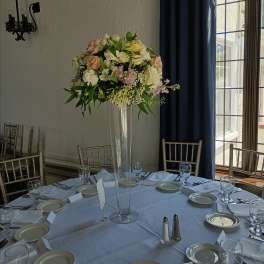 Tall floral centerpiece in a clear glass vase on a set dining table