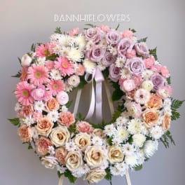 Heart-shaped floral wreath with pink, lavender, peach, and white blooms on an easel