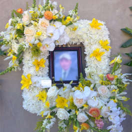 Large white and yellow floral funeral wreath on an easel with a framed photo in the center