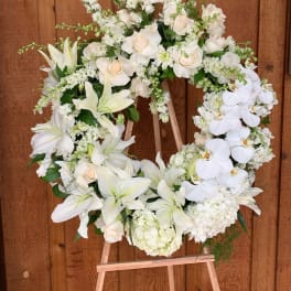 White floral wreath on a wooden easel with lilies, roses, and orchids