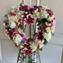 Heart-shaped floral wreath on a wooden easel with pink, white, and purple blooms