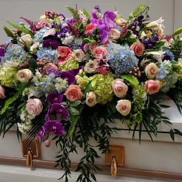 Large multicolored casket spray with roses, hydrangeas, lilies, and orchids on a white casket