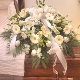 White floral casket spray with lilies, roses, and ribbon