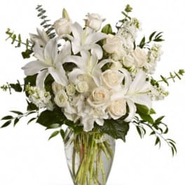 Tall arrangement of white lilies and roses in a clear glass vase