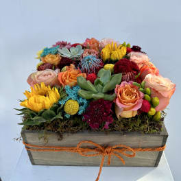 Colorful mixed flower arrangement in a wooden box with an orange ribbon