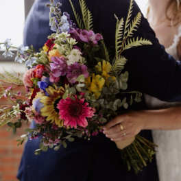 Couple holding a colorful mixed bouquet with sunflowers and gerbera daisies