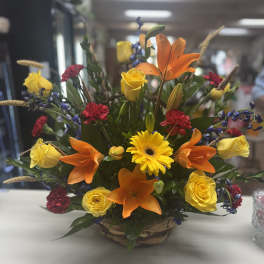 Mixed bouquet with orange lilies, yellow roses, and a yellow gerbera daisy in a basket