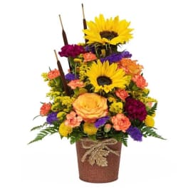 Tiered floral arrangement with sunflowers, roses, and carnations in a burlap-wrapped pot
