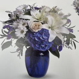 White lilies and purple flowers arranged in a blue glass vase