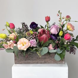 Mixed bouquet of tulips, roses, and protea in a wooden box