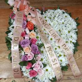 Heart-shaped floral tribute with pink roses and white daisies, tied with satin ribbons