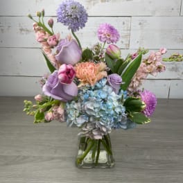 Pastel bouquet of roses, hydrangeas, and mixed blooms in a clear glass vase