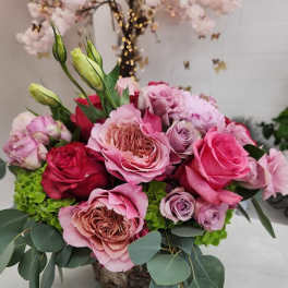 Low arrangement of pink and red roses with green hydrangea in a rustic container