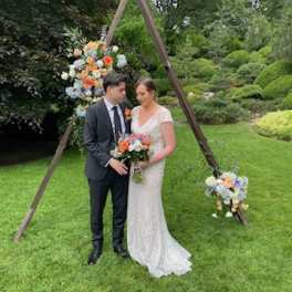 Bride and groom with colorful wedding flowers under a wooden arch