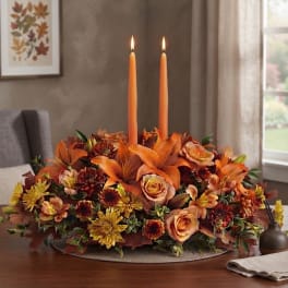 Orange floral centerpiece with two tall taper candles