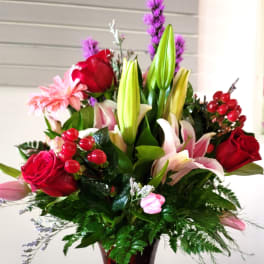 Mixed bouquet of lilies, roses, and pink daisies in a red glass vase