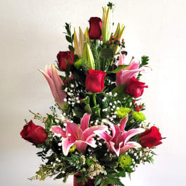 Tall bouquet of red roses and pink lilies in a red glass vase