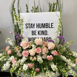 Large floral arrangement with a sign reading "STAY HUMBLE. BE KIND. WORK HARD."