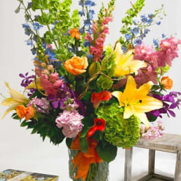 Tall mixed bouquet with lilies, roses, orchids, and blue flowers in a glass vase