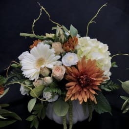 Mixed floral arrangement in a white pumpkin container with white, peach, and orange blooms