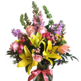 Mixed bouquet of yellow lilies, pink roses, and purple flowers in a glass vase