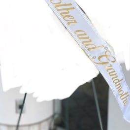White funeral ribbon with gold text draped across a floral spray