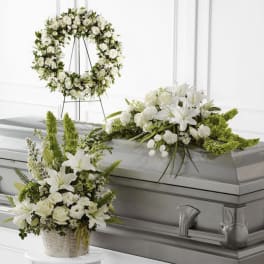 White funeral flowers arranged on a casket with a matching wreath and basket spray.