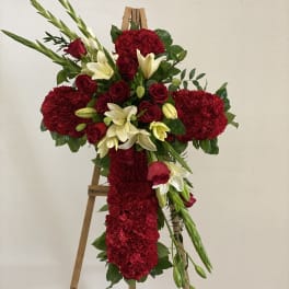 Red floral cross arrangement on a wooden easel with white lilies and roses