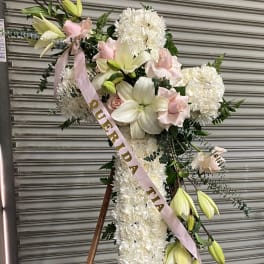 Standing floral cross with white flowers, lilies, and pink ribbon on an easel