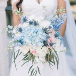 Bride holding a pastel blue and white bouquet with roses and thistle