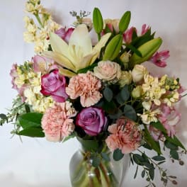Pastel bouquet of lilies, roses, carnations, and mixed flowers arranged in a clear glass vase