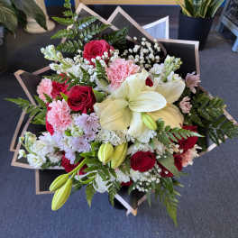 Bouquet of red roses, white lilies, and pink carnations wrapped in black paper