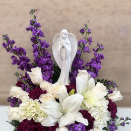 White lilies and roses with purple flowers around a white angel figurine