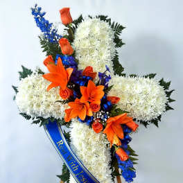 Cross-shaped floral tribute with white chrysanthemums, orange lilies, and blue ribbon