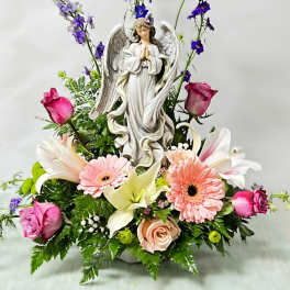 Angel figurine surrounded by pink roses, lilies, gerberas, and purple flowers