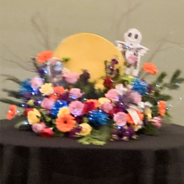 Colorful floral arrangement with a small skeleton figure and a yellow circle backdrop