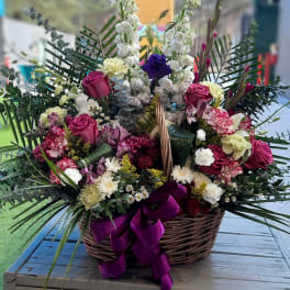 Large basket arrangement with pink roses and white flowers, tied with a purple ribbon