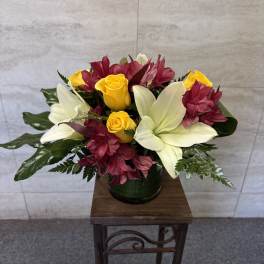 Bouquet of yellow roses and white lilies with burgundy flowers in a dark vase