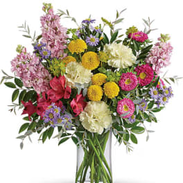 Mixed bouquet of pink, yellow, white, and purple flowers in a clear glass vase