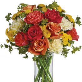 Mixed bouquet of roses, carnations, and yellow button flowers in a clear vase