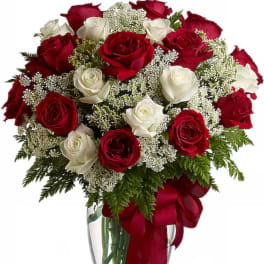Red and white roses arranged in a clear glass vase with a red ribbon