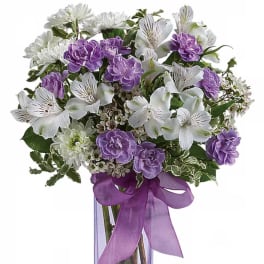 Purple and white flower bouquet in a clear vase with a purple ribbon